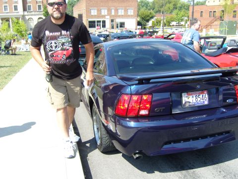 2007 Ford Mustang - A man stands by a Ford Mustang GT at an outdoor car event. Other vehicles are visible in the background.