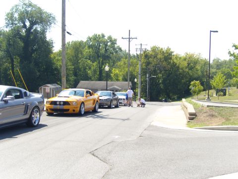 2007 Ford Mustang - Several Ford Mustangs are parked on a street, with people gathered around one of the cars.