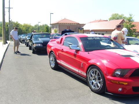 2007 Ford Mustang - A red Shelby Mustang is parked in a line of cars, with people standing around.