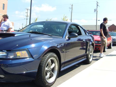 2007 Ford Mustang - A blue Ford Mustang GT is parked in a line with other vehicles, with a person standing nearby.