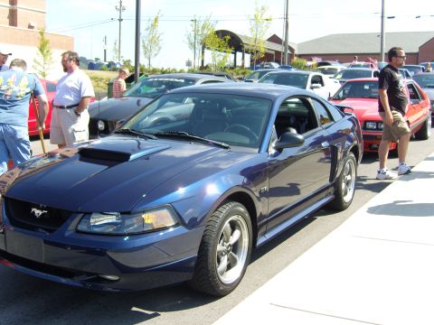 2007 Ford Mustang - A blue 2007 Ford Mustang GT is parked on the street, with other vehicles and people visible in the background.