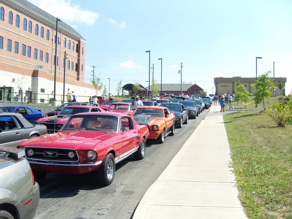 Red 1967 Ford Mustang in a line of cars, front 3/4 view, slight damage on front bumper