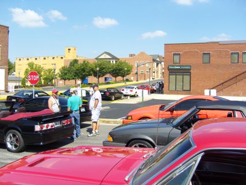 2007 Ford Mustang - Several convertibles, including a red, orange, and gray model, are parked on a street during a car show.
