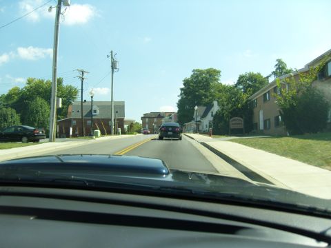 2007 Ford Mustang - A dark sedan is seen driving down a street lined with trees and buildings on a sunny day.