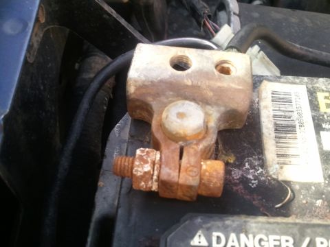 1994 Ford Bronco - A close-up view of a heavily corroded battery terminal clamp attached to a car battery, with visible rust and oxidation.