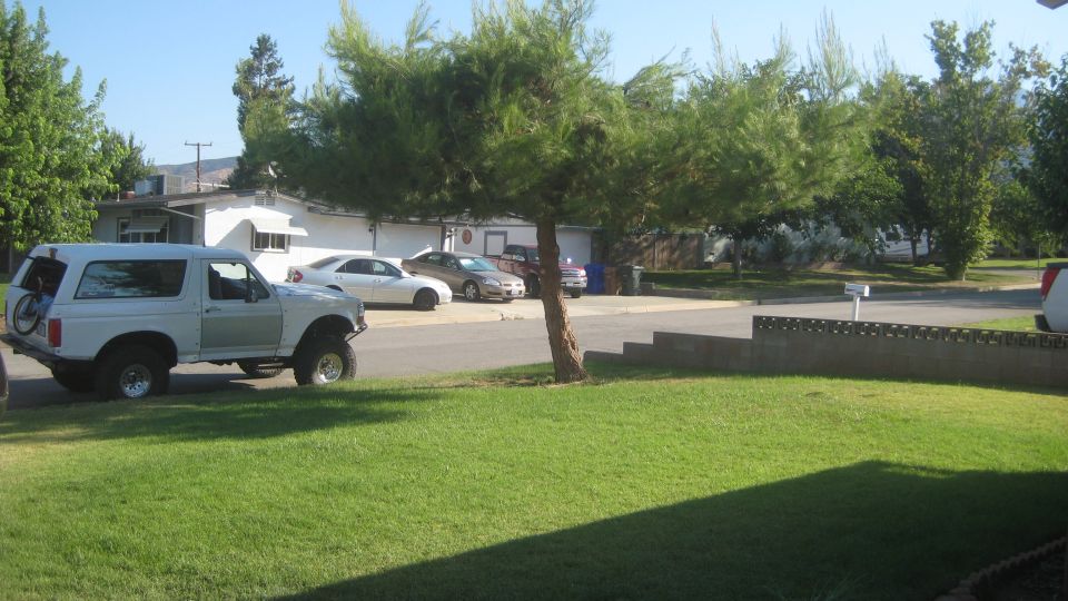White Ford Bronco parked on the street, bicycle mounted on rear carrier. Other cars parked in driveway