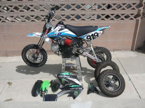 1988 Ford Bronco - A dirt bike is displayed on a stand with various spare parts laid out on the ground, including fenders and wheels.