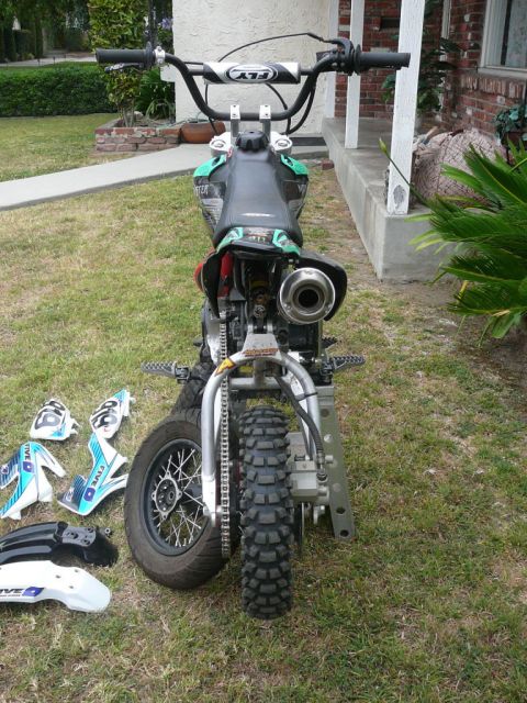 1988 Ford Bronco - A dirt bike is shown from the rear, with its front wheel and handlebars visible. Several body panels are detached and placed on the lawn.