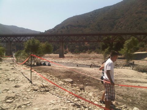 1986 Ford Bronco - A dry riverbed scene with a large bridge in the background and people gathered near caution tape.