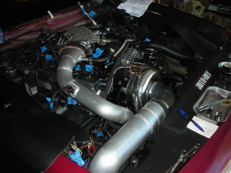 engine bay with large turbocharger and custom intake piping, some parts marked with blue tape