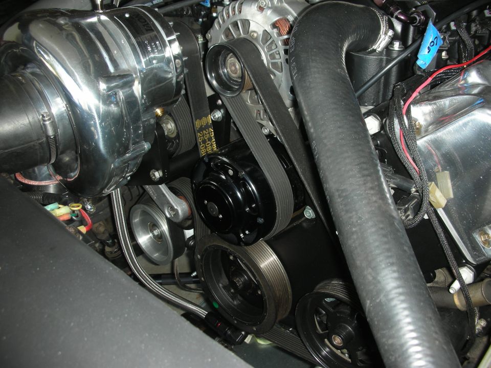 Close-up of a polished supercharger, alternator, belts, and pulleys on an engine
