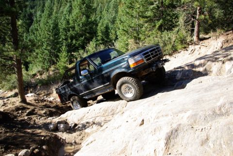 1995 Ford Bronco - A dark green 1992 Ford Bronco navigates a challenging off-road course on a sunny day.