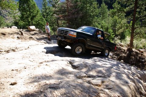 1995 Ford Bronco - A 1995 Ford Bronco navigates a rocky off-road trail with a driver and passenger visible.