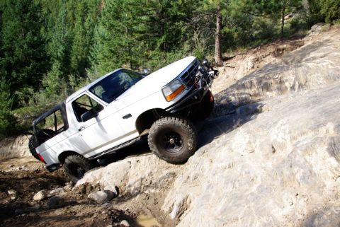 1995 Ford Bronco - White Ford Bronco navigates a challenging rocky trail in a wooded area.