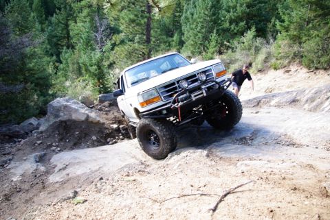1995 Ford Bronco - A modified white SUV navigates a challenging rocky terrain on an off-road trail.