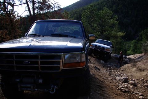 1995 Ford Bronco - Two SUVs navigate a challenging rocky trail in a wooded mountain area.