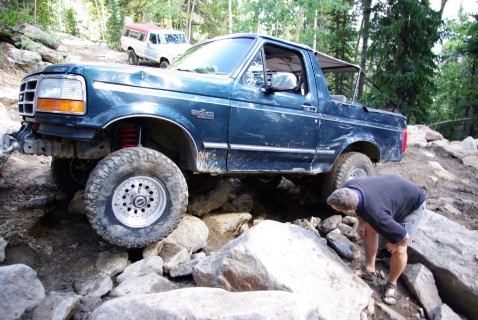 Dark blue 1992 Ford Bronco with off-road modifications navigating rocky terrain