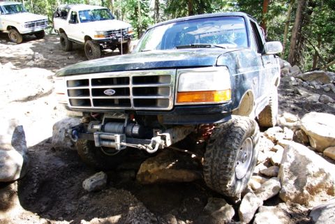 1995 Ford Bronco - A dark blue 1995 Ford Bronco tackles a challenging off-road trail, with two other Broncos visible in the background.