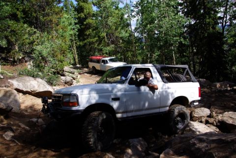 1995 Ford Bronco - A white Ford Bronco tackles a challenging off-road course with another vehicle in the background.