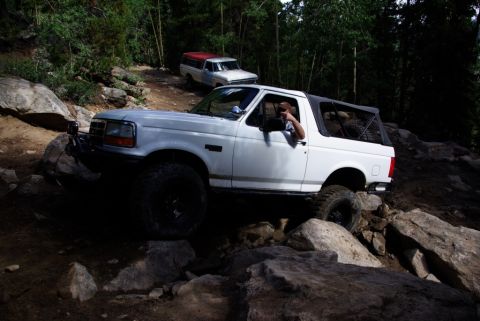 1995 Ford Bronco - 1995 Ford Bronco tackling a challenging off-road course with a second vehicle in the background.