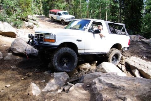 1995 Ford Bronco - Two off-road vehicles tackle a challenging rocky path in a wooded area.