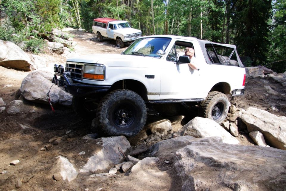 White SUV navigating a rocky trail, with a white pickup truck behind it
