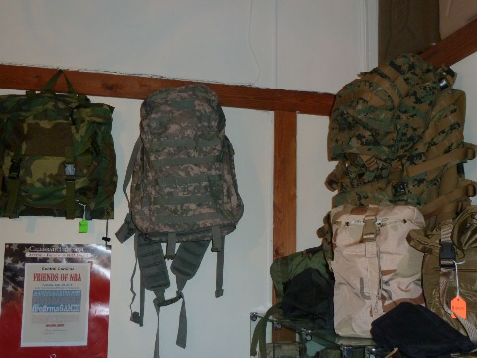 Several camouflage backpacks hang on a wall next to a poster
