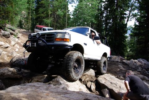 1995 Ford Bronco - 1995 Ford Bronco tackling a challenging off-road course in a wooded area.