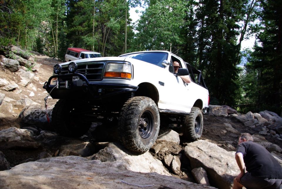 White 1995 Ford Bronco navigating a steep, rocky trail with another vehicle visible in the background