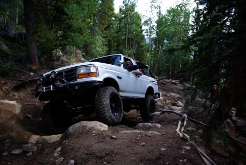 1995 Ford Bronco - A white 1995 Ford Bronco navigates a challenging rocky trail in a forest setting.