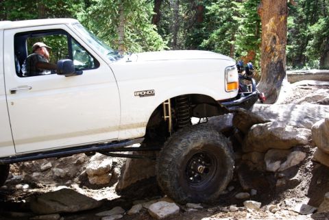 1995 Ford Bronco - A white 1995 Ford Bronco navigates a rocky trail, demonstrating its off-road capabilities with a lifted suspension and aggressive tires.
