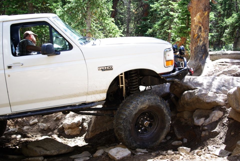 White 1995 Ford Bronco off-roading over rocks, showing its lifted suspension and large tires