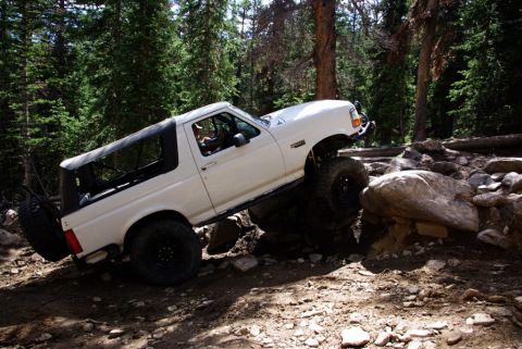 1995 Ford Bronco - This 1995 Ford Bronco is shown off-roading on a challenging, rocky path surrounded by trees.