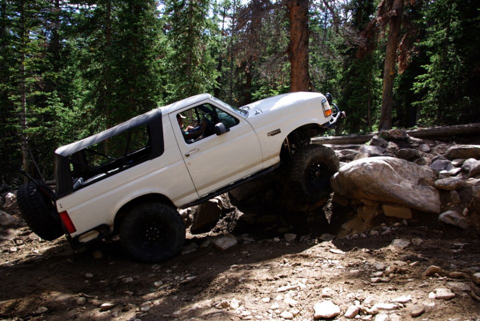 White 1995 Ford Bronco navigating rocky terrain on a wooded trail