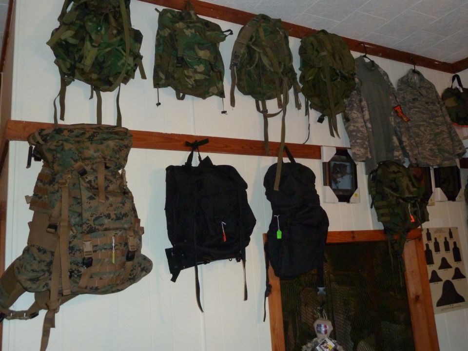Various camouflage and black backpacks hanging on a wooden rack