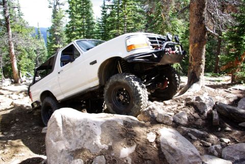 1995 Ford Bronco - 1995 Ford Bronco navigating a challenging off-road course with large boulders and trees.