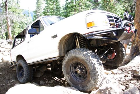 1995 Ford Bronco - This 1995 Ford Bronco is navigating a challenging, rocky off-road trail with its suspension clearly visible.
