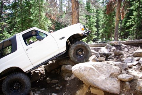 1995 Ford Bronco - A white 1995 Ford Bronco navigates a rocky trail in a forest setting.