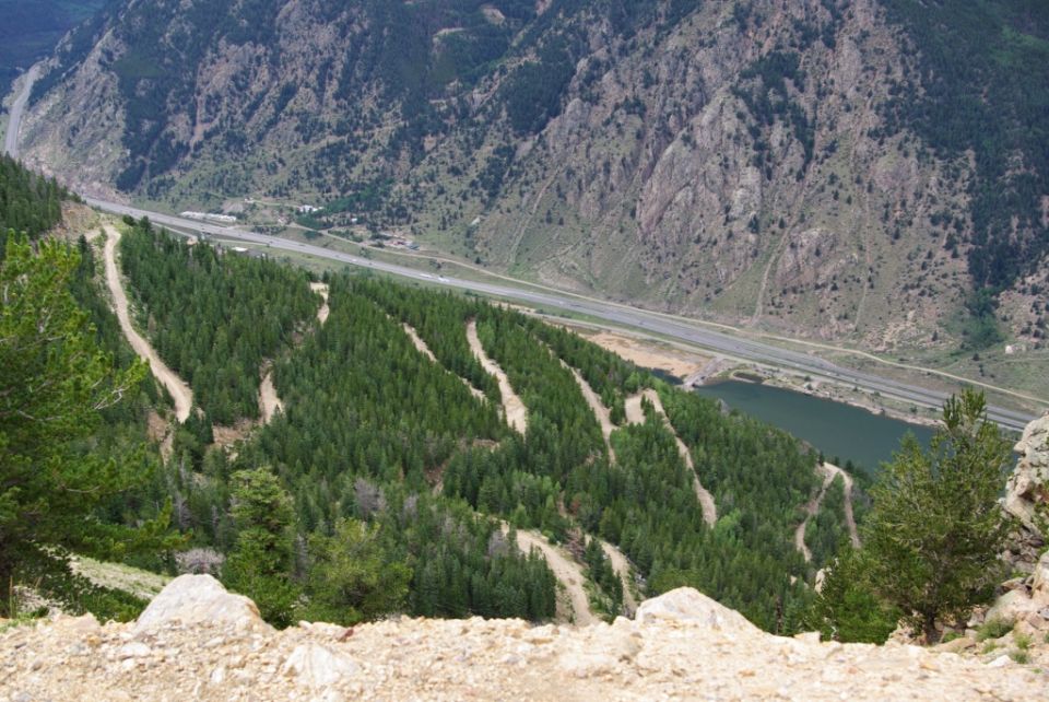 Mountain landscape with winding dirt roads and a highway next to a lake