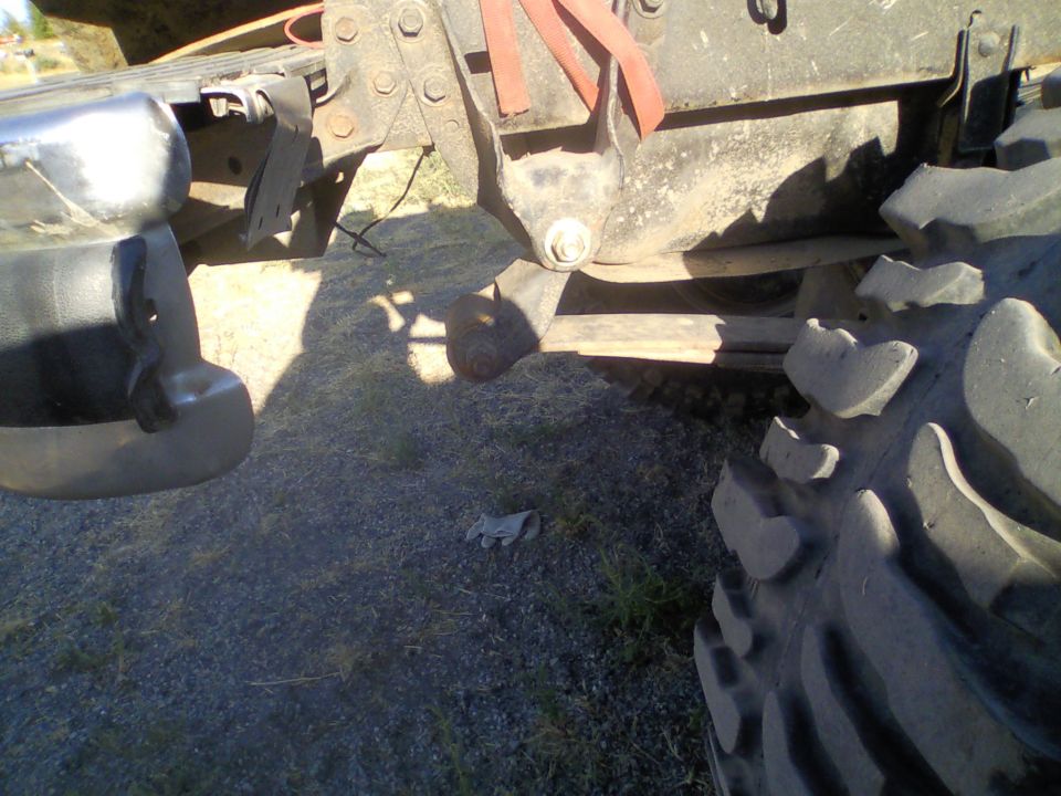 Close-up of a large, knobby tire and suspension components of a vehicle, with a chrome bumper visible on the left