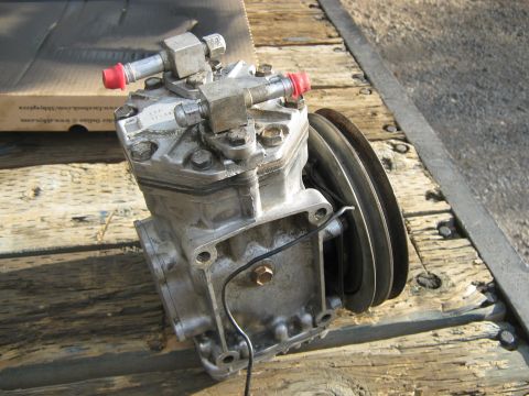 1972 Ford F-250 - An air conditioning compressor part is shown resting on wooden planks, with visible tubing and a pulley.