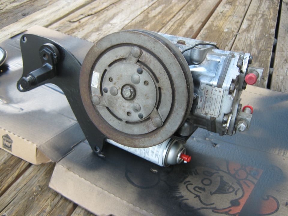 Air conditioning compressor with mounting bracket and pulley, resting on cardboard