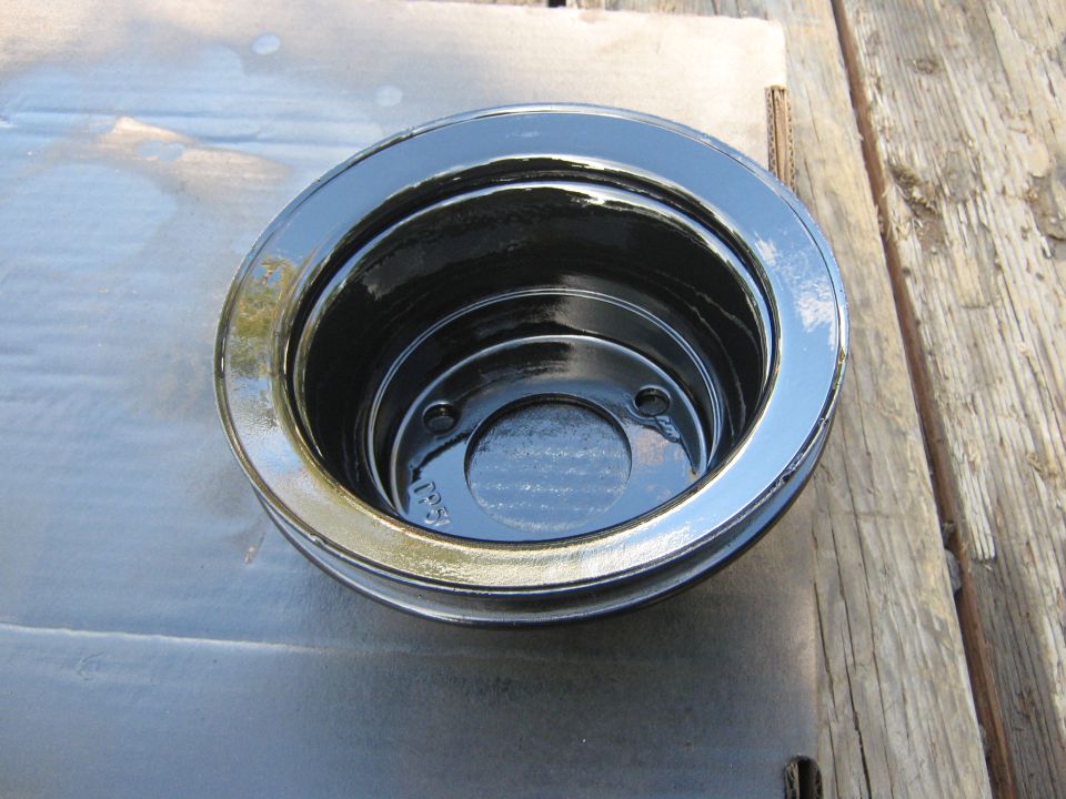 Black crankshaft pulley with two grooves, resting on a wooden surface. Some oil is visible