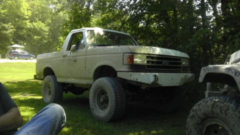 1989 Ford Bronco - A lifted tan Ford Bronco is parked on grass next to another off-road vehicle.