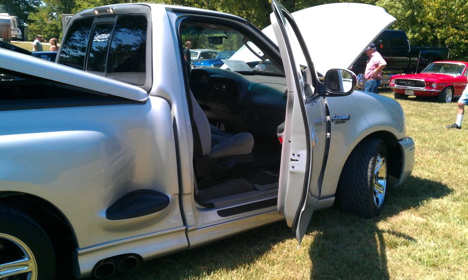 Silver pickup truck with driver's door open, showing interior. Chrome wheels and dual exhaust pipes visible