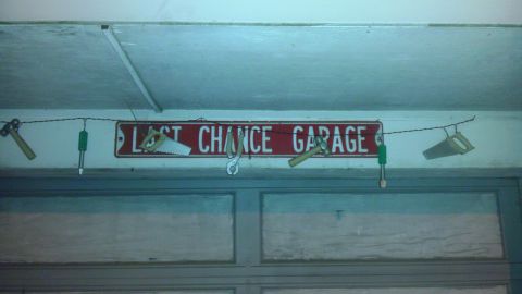 1989 Ford Bronco - A sign reading "LAST CHANCE GARAGE" is displayed above a garage door, adorned with various tools.