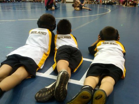 1987 Ford Bronco - Three young athletes in matching uniforms lie on the mat, observing a wrestling competition.
