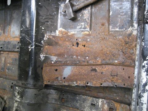 1973 Ford Ranchero - Close-up of a heavily rusted car floor pan, showing damage and a hammer.