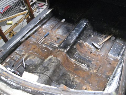 1973 Ford Ranchero - The interior floor of a vehicle shows significant rust and is littered with tools.