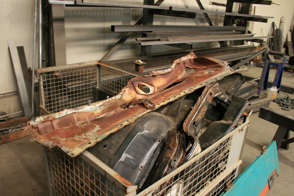 Rusted car floor pan and fender parts in a wire basket, some black parts visible